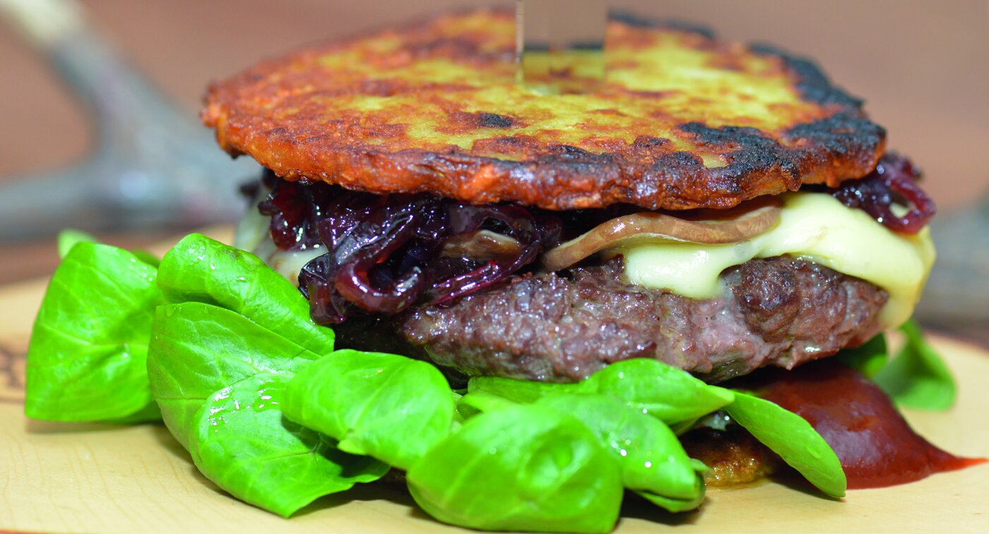 WilderBurger, angerichtet mit Zwiebelmarmelade, Camembert und Feldsalat